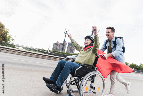 Young man pushing senior man sitting in a wheelchair dressed up as superhero photo