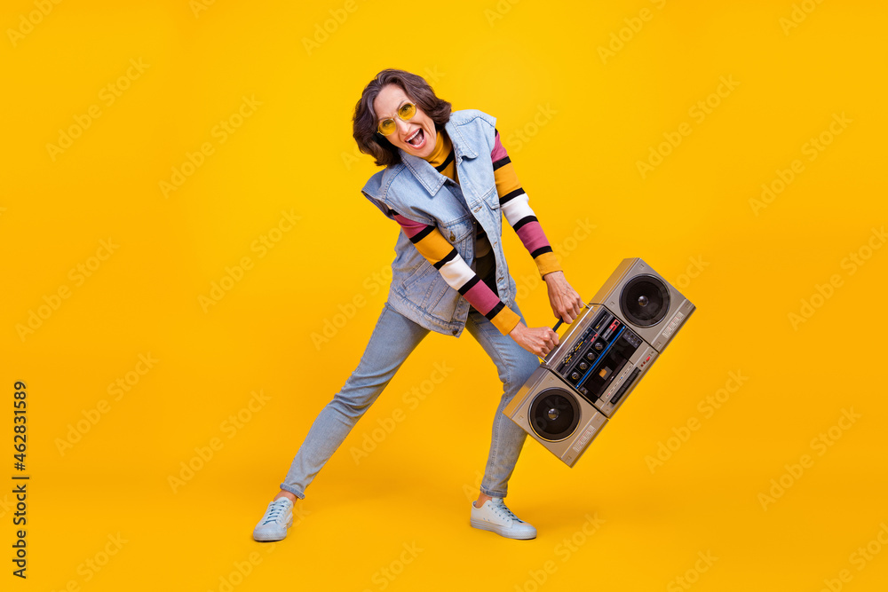 Full size photo of crazy white hairdo old lady hold boom box dance wear eyewear sweater vest jeans shoes isolated on yellow background Full size photo of crazy white hairdo old lady hold boom box dance wear eyewear sweater vest jeans shoes isolated on yellow background