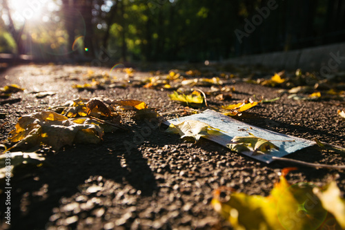 Medical face mask lying on asphalt with autumn leaves outdoors