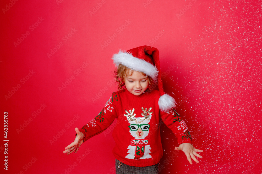 little girl in Santa hat blowing on snow red background Studio