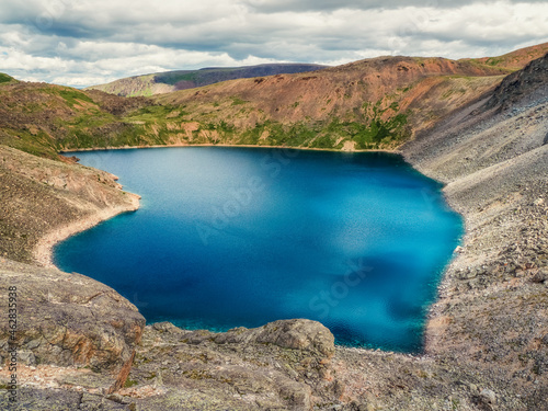Blue mountain lake in the caldera. Mountain range against a cloudy sky. Caldera of an extinct volcano is surrounded by a mountain range. In the valley there is a blue lake with steep rocky shores.