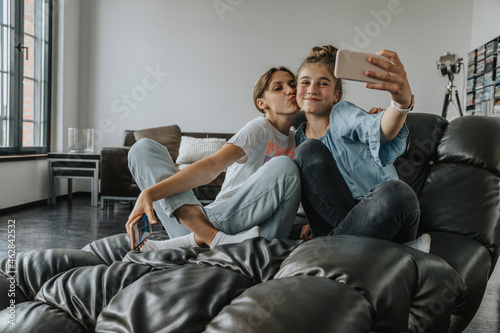 Friends taking selfie with smart phone while sitting on couch at home photo