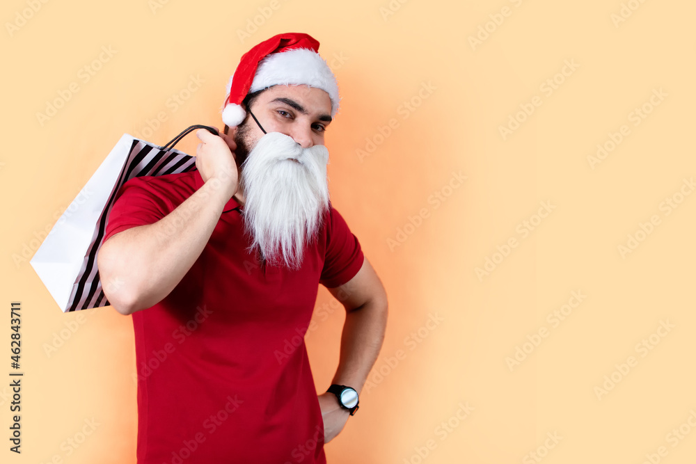 Young man with Santa Claus hat and white beard, with shopping bags. Front view. Young man with Santa Claus hat and white beard, with shopping bags. Front view.