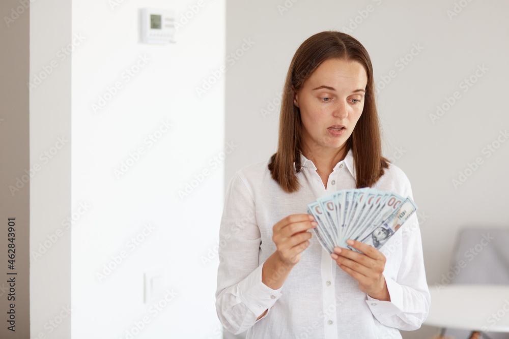Portrait of astonished young adult beautiful girl wearing white casual style shirt, standing holding big sum of money, having surprised facial expression. Portrait of astonished young adult beautiful girl wearing white casual style shirt, standing holding big sum of money, having surprised facial expression.