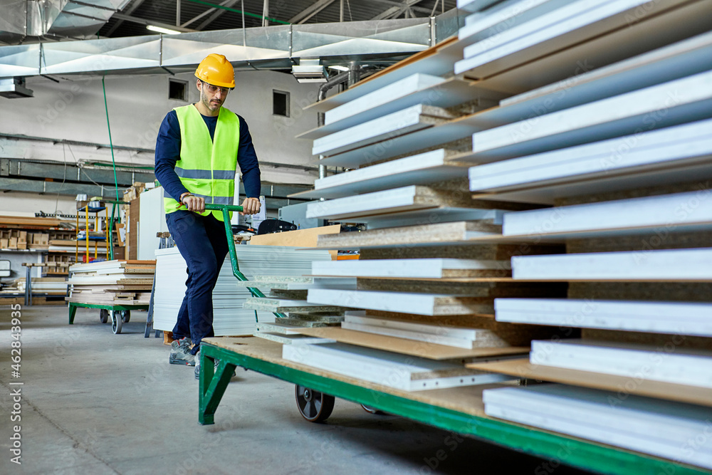 Worker pulling pallet jack with wooden boards in factory Stock Photo