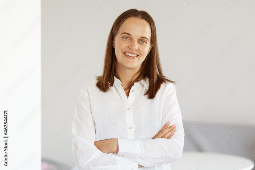 Happy satisfied optimistic winsome female with pleasant appearance wearing white casual style shirt standing with crossed hands, expressing confidence, looking at camera. Happy satisfied optimistic winsome female with pleasant appearance wearing white casual style shirt standing with crossed hands, expressing confidence, looking at camera.