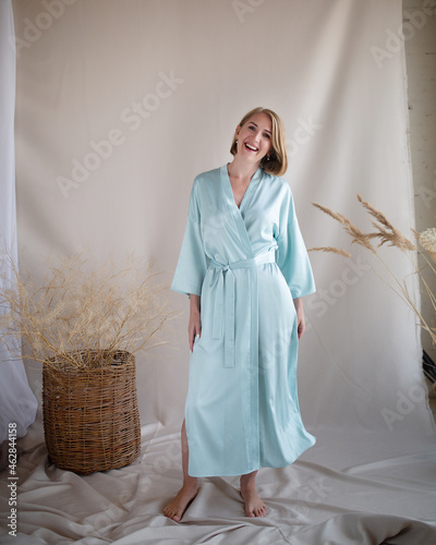 Full length portrait of beautiful young woman wearing elegant long turquoise silk robe sitting on stool barefoot