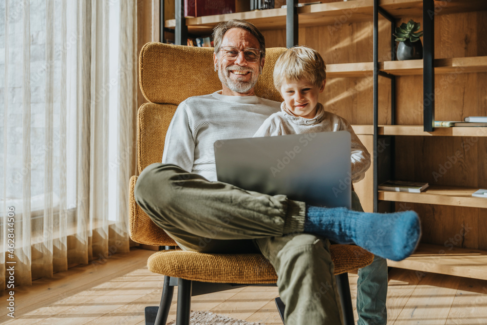Smiling boy using laptop while sitting with father on chair Stock Photo ...