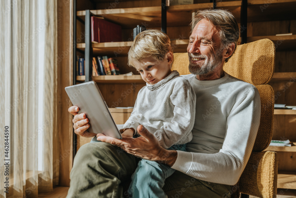 Boy e-learning while sitting on smiling father's lap in living room