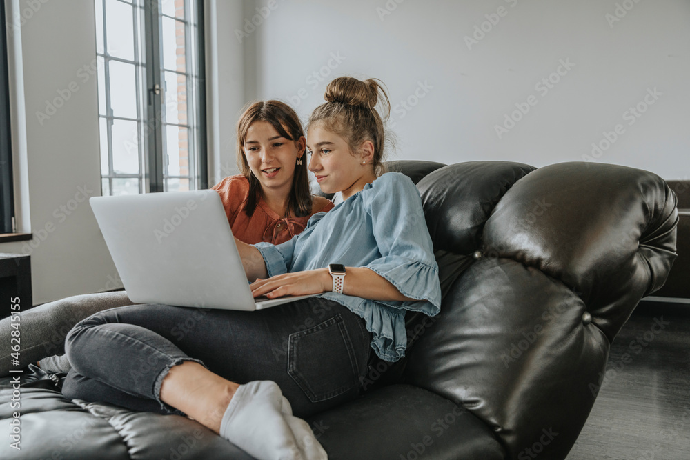 Friends using laptop while relaxing on sofa at home Friends using laptop while relaxing on sofa at home