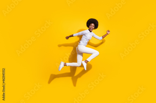 Full length profile side photo of trendy brunette afro american girl jump up run isolated on yellow color background