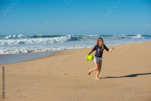 cute young girl playing and running on the beach with her toys