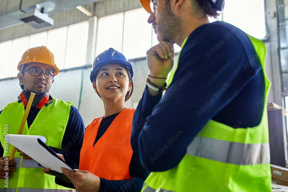 Two men and woman in reflective vests discussing in factory Two men and woman in reflective vests discussing in factory