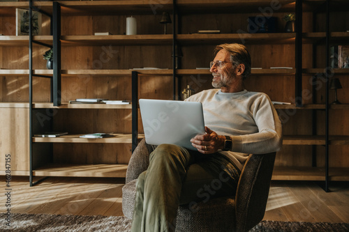 Smiling mature man with laptop sitting on armchair photo