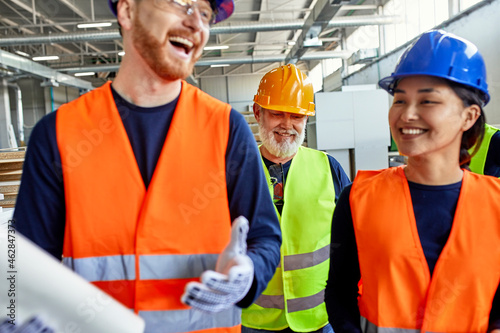 Happy colleagues in protective workwear talking in factory photo