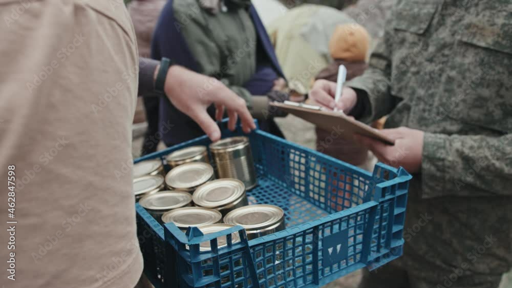 Midsection shot of social worker giving tinned food to diverse men and women living at tent city while police officer in military uniform taking notes on clipboard Midsection shot of social worker giving tinned food to diverse men and women living at tent city while police officer in military uniform taking notes on clipboard