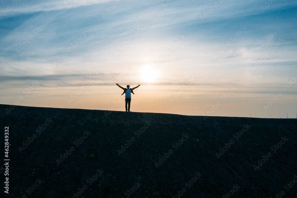 Businessman standing with arms outstretched on hill against sky during sunset Businessman standing with arms outstretched on hill against sky during sunset