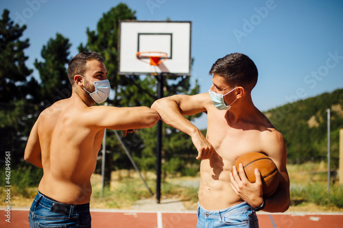 Athletes with face mask greeting with elbow bump at basketball court photo