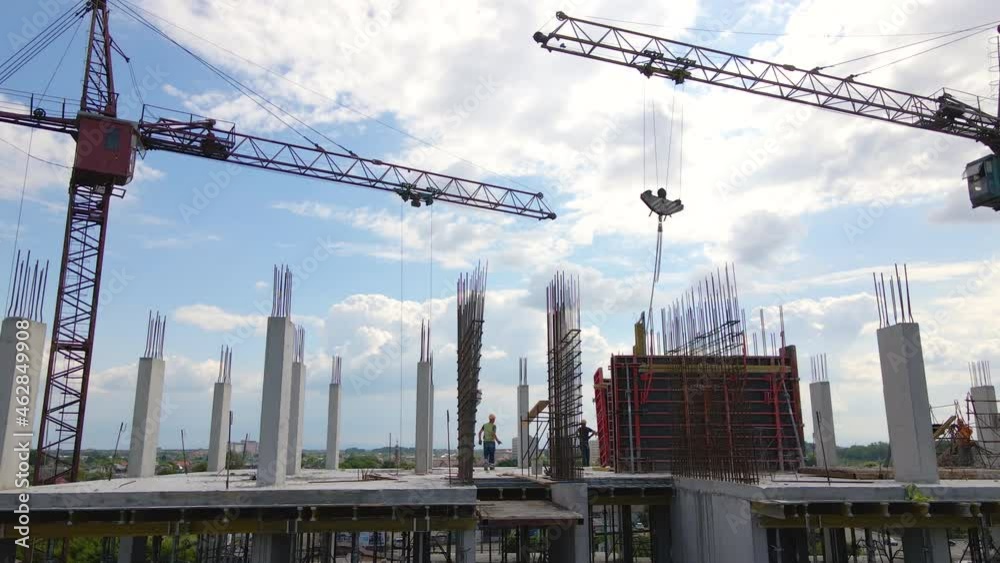 Tower cranes and workers at high concrete residential building under construction. Real estate development concept.
