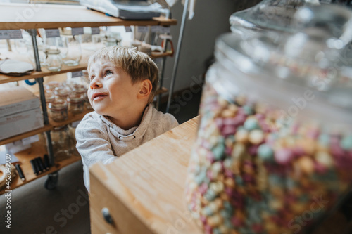 Blond little boy day dreaming while standing in candy store photo