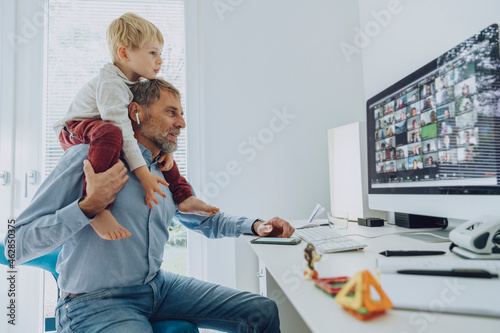 Father carrying son on shoulder while attending video conference at home office