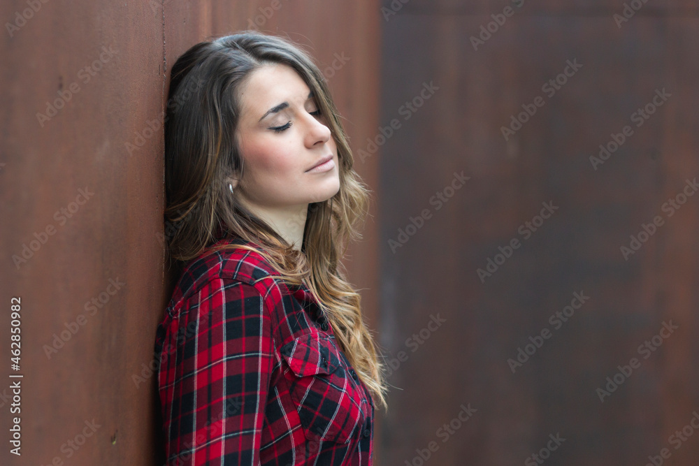 Portrait of young woman wearing red plaid shirt leaning against brown wall Portrait of young woman wearing red plaid shirt leaning against brown wall