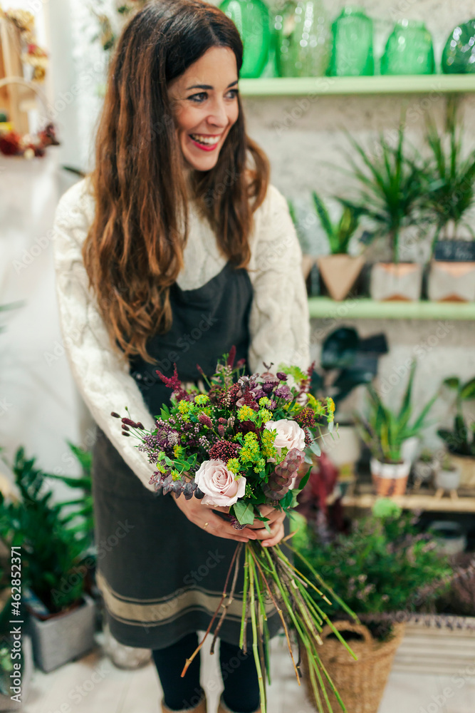 Smiling woman holding bunch of flowers while standing at flower shop Smiling woman holding bunch of flowers while standing at flower shop