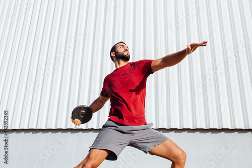 Young man practicing disc throw while standing against wall photo