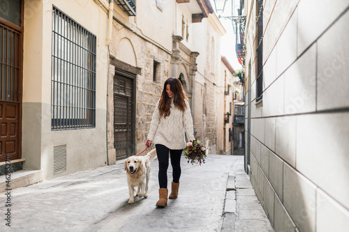 Woman holding bouquet while walking with dog on road in city photo