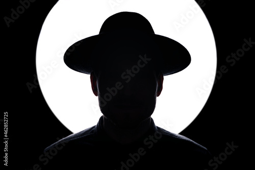 In silhouette of man wearing hat standing against illuminated lighting equipment photo
