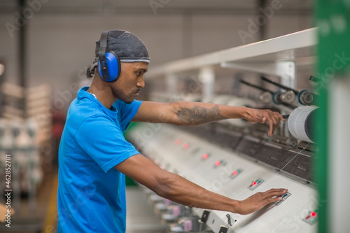 Man wearing ear defenders operating machine in factory photo
