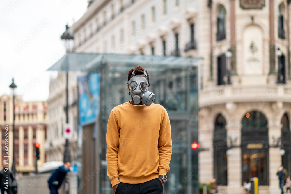 Young man with hands in pockets and gas mask standing in city