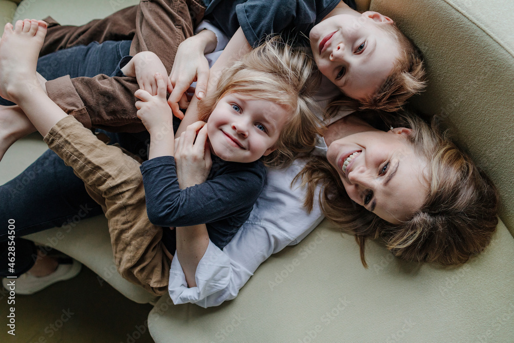 High angle view of happy mother lying with sons on sofa in living room at home High angle view of happy mother lying with sons on sofa in living room at home