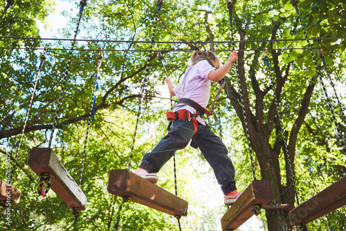 Portrait of brave little girl walk on a rope bridge in an adventure rope park. Having fun at adventure park. Scout practicing rappelling
