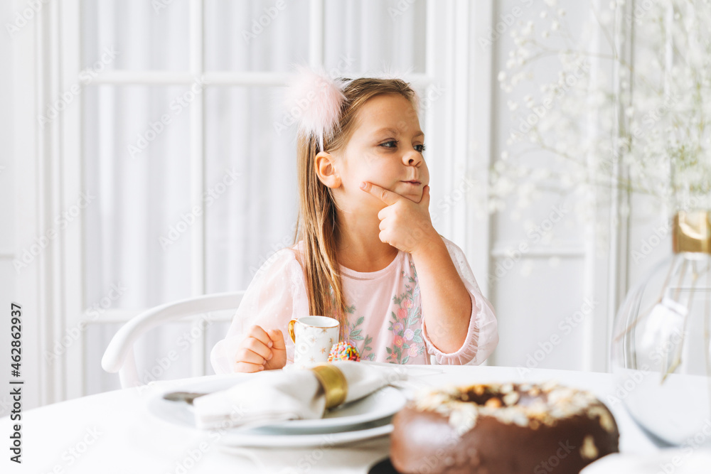 Funny cute little girl with long hair in light pink dress with chocolate cake in hands on festive table in bright living room at home. Christmas time, birthday girl Funny cute little girl with long hair in light pink dress with chocolate cake in hands on festive table in bright living room at home. Christmas time, birthday girl