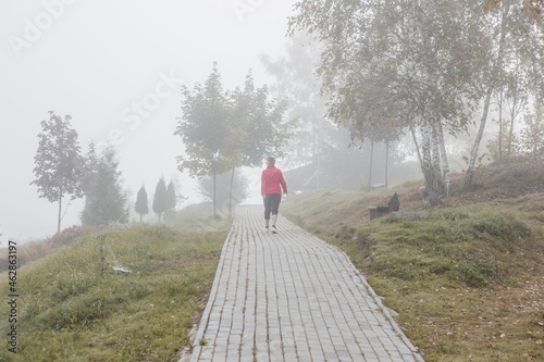 Autumn outdoor active lifestyle. Fit sport .retired woman running in city park training cardio in nature path. Happy person exercising outdoors in yellow leaves foliage. photo