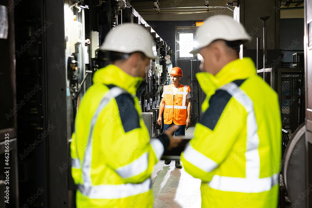 Back View of Two Engineers Stand in Electric Power Station, Use Digital Tablet Computer, Have Discussion. Energy Business Technology Industry Concept. Back View of Two Engineers Stand in Electric Power Station, Use Digital Tablet Computer, Have Discussion. Energy Business Technology Industry Concept.