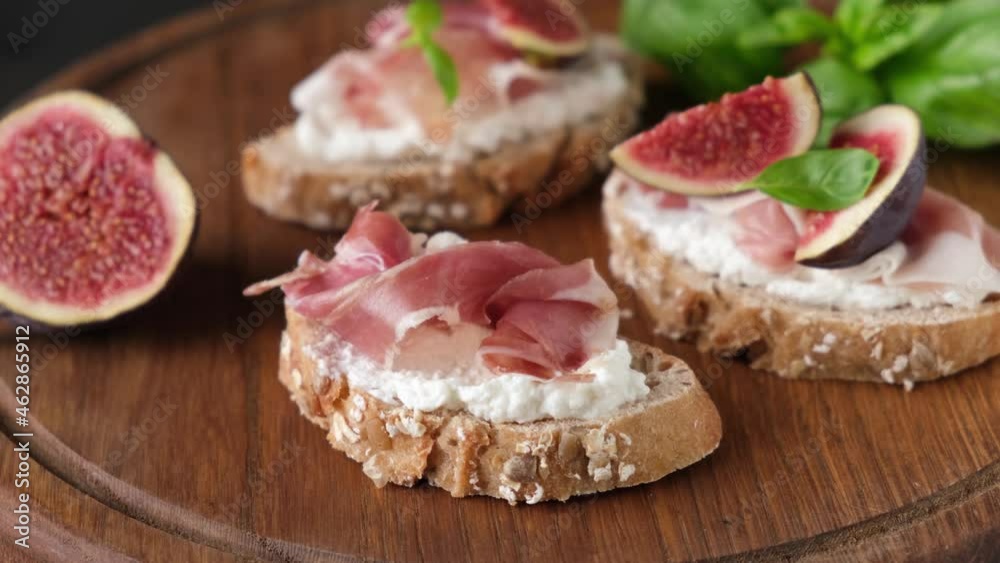 Female hands preparing bruschetta with ricotta cheese, figs and prosciutto Female hands preparing bruschetta with ricotta cheese, figs and prosciutto