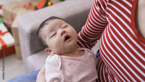 female cradling an adorable baby girl in her arms who is in a deep sleep and breathing with mouth during daytime at home.