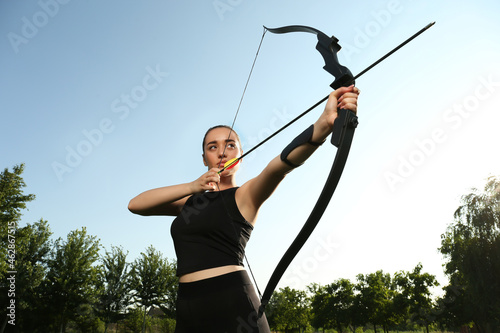 Tela Woman with bow and arrow practicing archery outdoors, low angle view