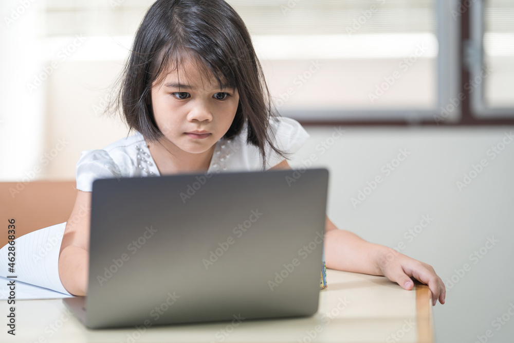 Asian children girl student writing on notebook while studying online via laptop while at home. Education Concept Stock Photo Asian children girl student writing on notebook while studying online via laptop while at home. Education Concept Stock Photo