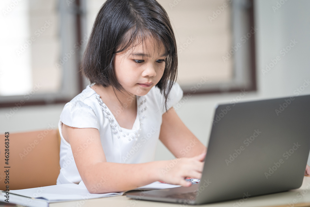 Asian children girl student writing on notebook while studying online via laptop while at home. Education Concept Stock Photo Asian children girl student writing on notebook while studying online via laptop while at home. Education Concept Stock Photo