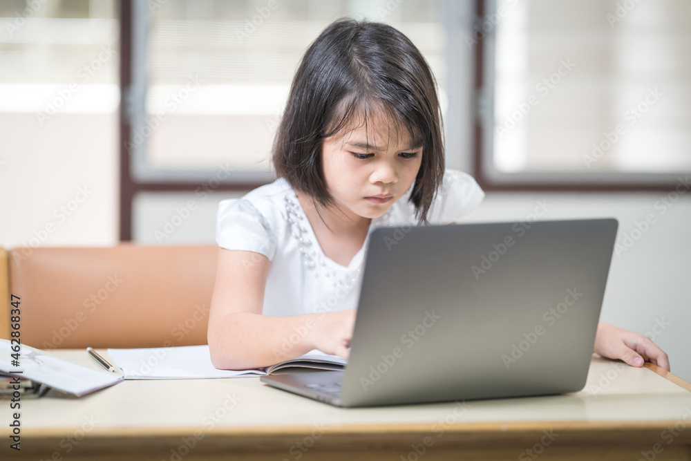 Asian children girl student writing on notebook while studying online via laptop while at home. Education Concept Stock Photo Asian children girl student writing on notebook while studying online via laptop while at home. Education Concept Stock Photo