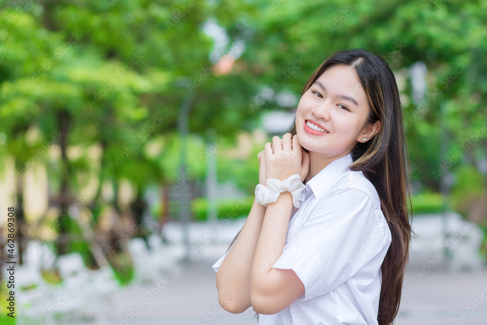 Beautiful young Asian woman student who has blond long hair smiles and looks at to camera while holding hands and standing in university with outdoor tree background. Beautiful young Asian woman student who has blond long hair smiles and looks at to camera while holding hands and standing in university with outdoor tree background.