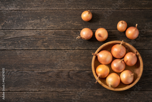 yellow onions in a wooden bowl on a rustic wooden table.