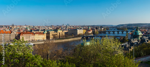 Wide panoramic aerial view of Prague Old Town architecture roof top and Charles Bridge over Vltava river seen from Letna hill park, spring sunny day, blue sky, Czech Republic
