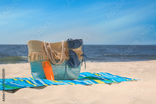 Striped beach towel and bag with accessories on sandy seashore