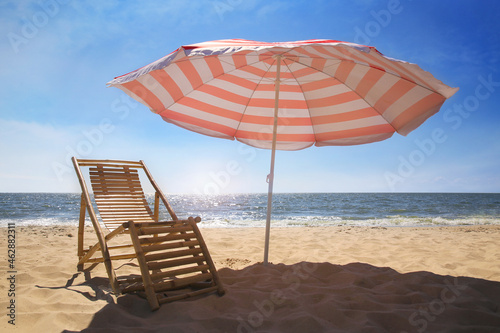 Deck chair near red and white striped beach umbrella on sandy seashore