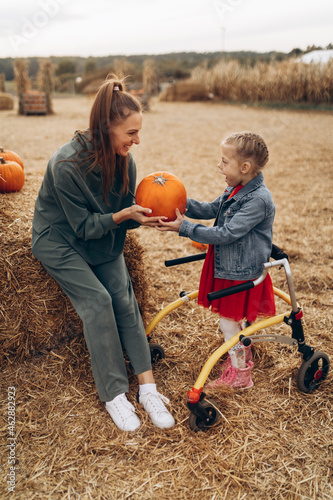 Mother and her disabled daughter spend time on a pumpkin field, they are holding a big pumpkin together.