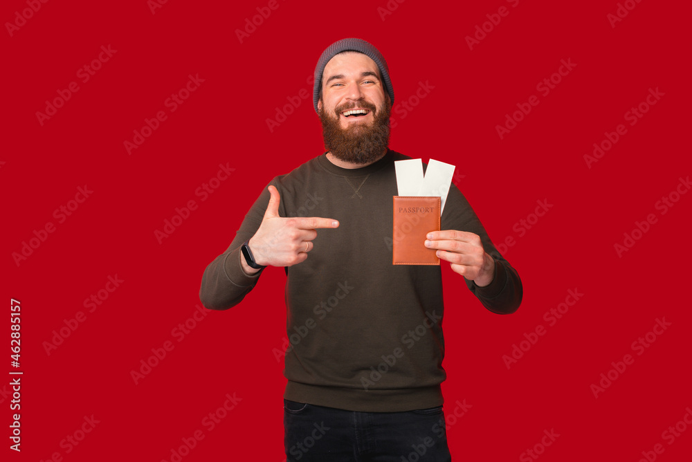 Wide smiling man is pointing at the passport with tickets he is holding. Wide smiling man is pointing at the passport with tickets he is holding.